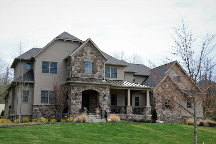 Stunning luxury home exterior entrance with natural stone veneer facade pedestals and manicured front lawn curb appeal